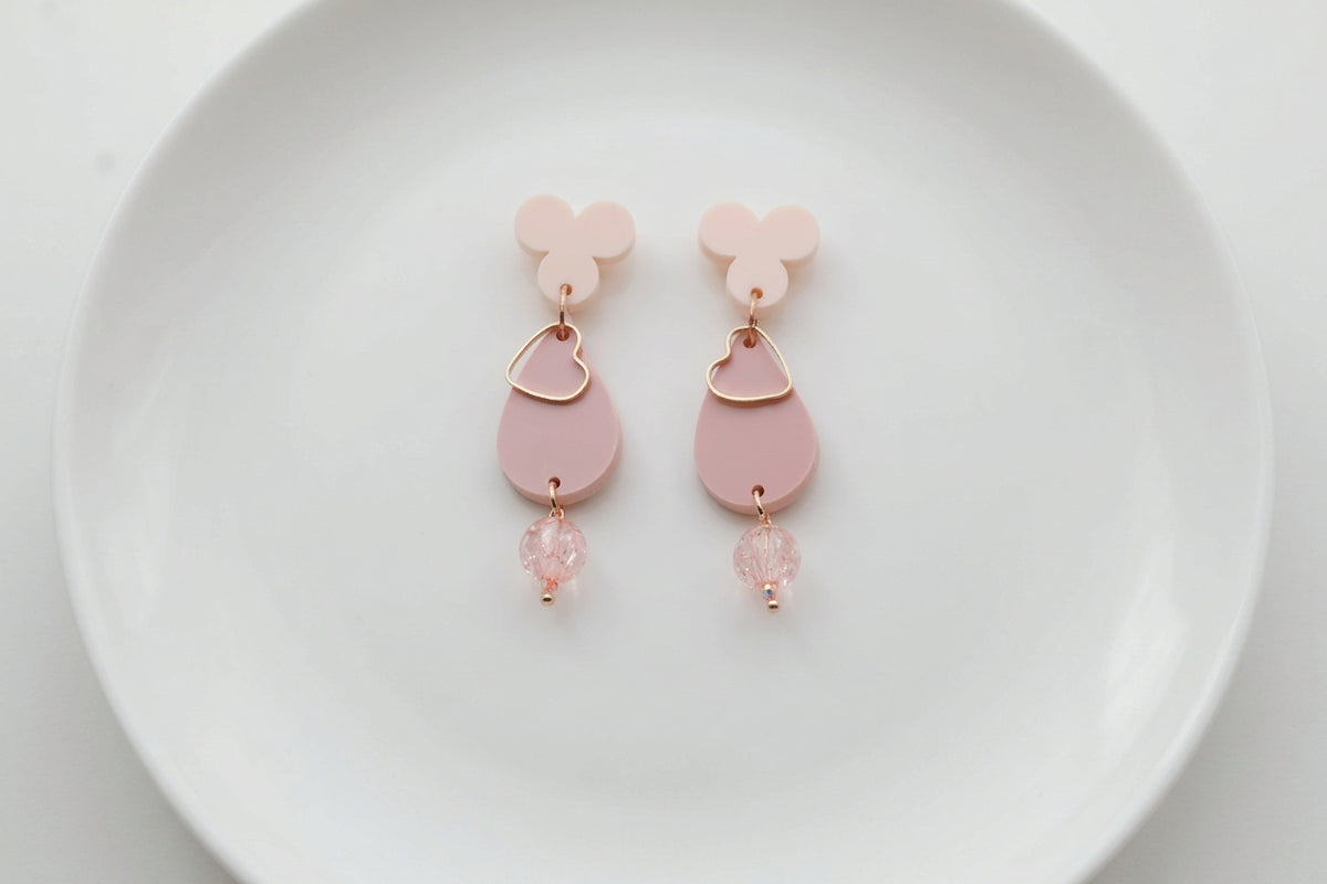 Beige Ana teardrop acrylic dangle earrings arranged on a white plate