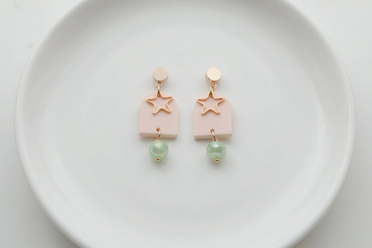 Beige Eira star acrylic drop earrings arranged on a white plate