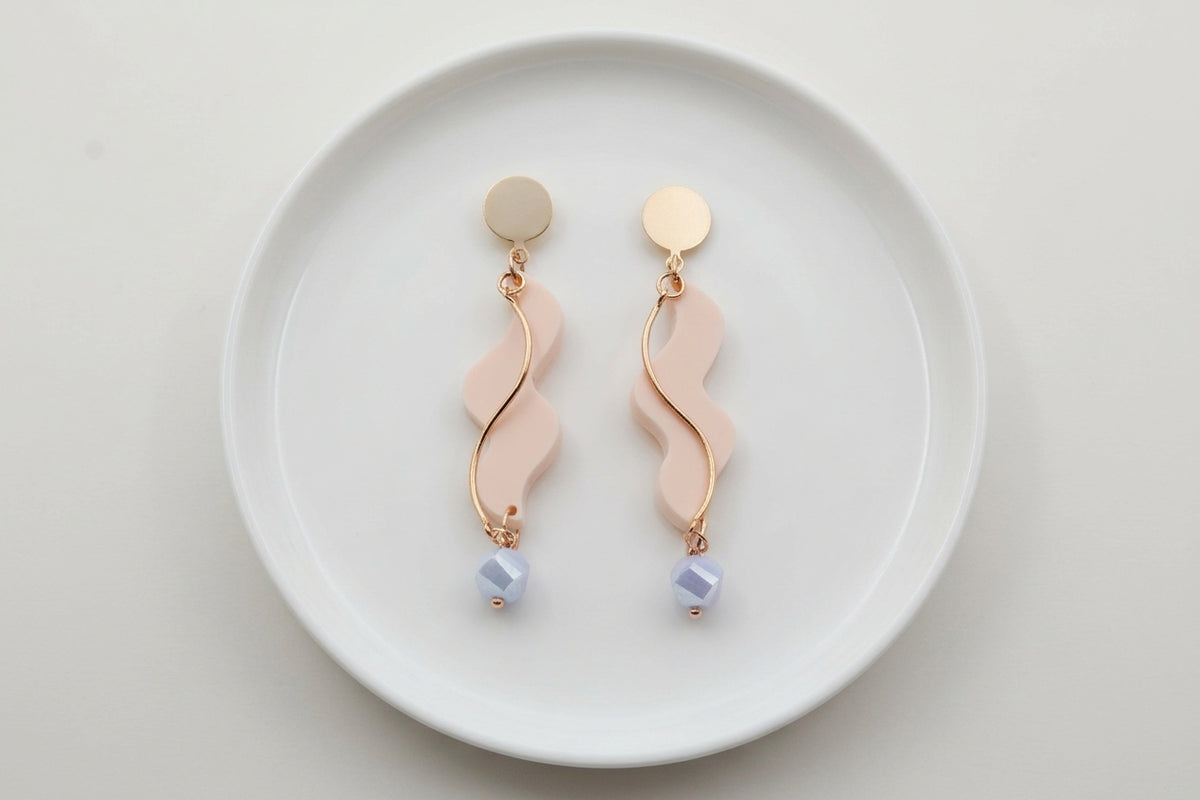 Beige Esme long acrylic statement earrings arranged on a white plate