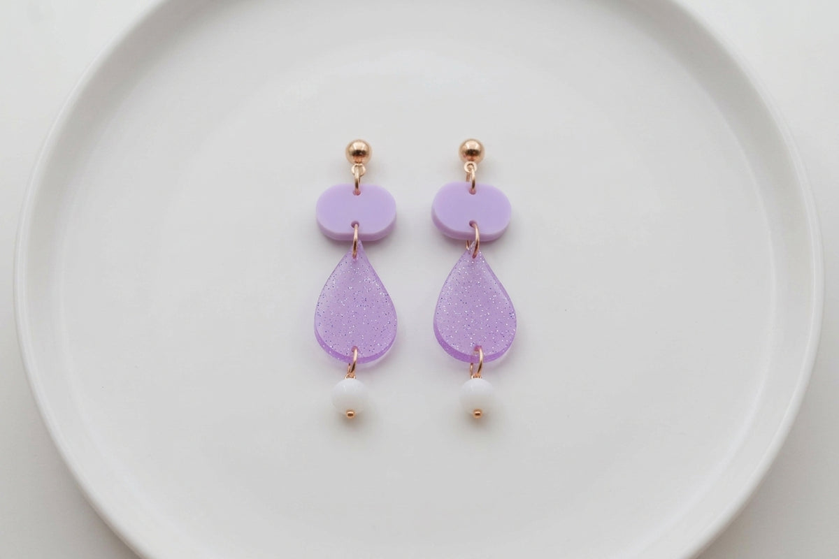 Purple Noor teardrop acrylic drop earrings arranged on a white plate