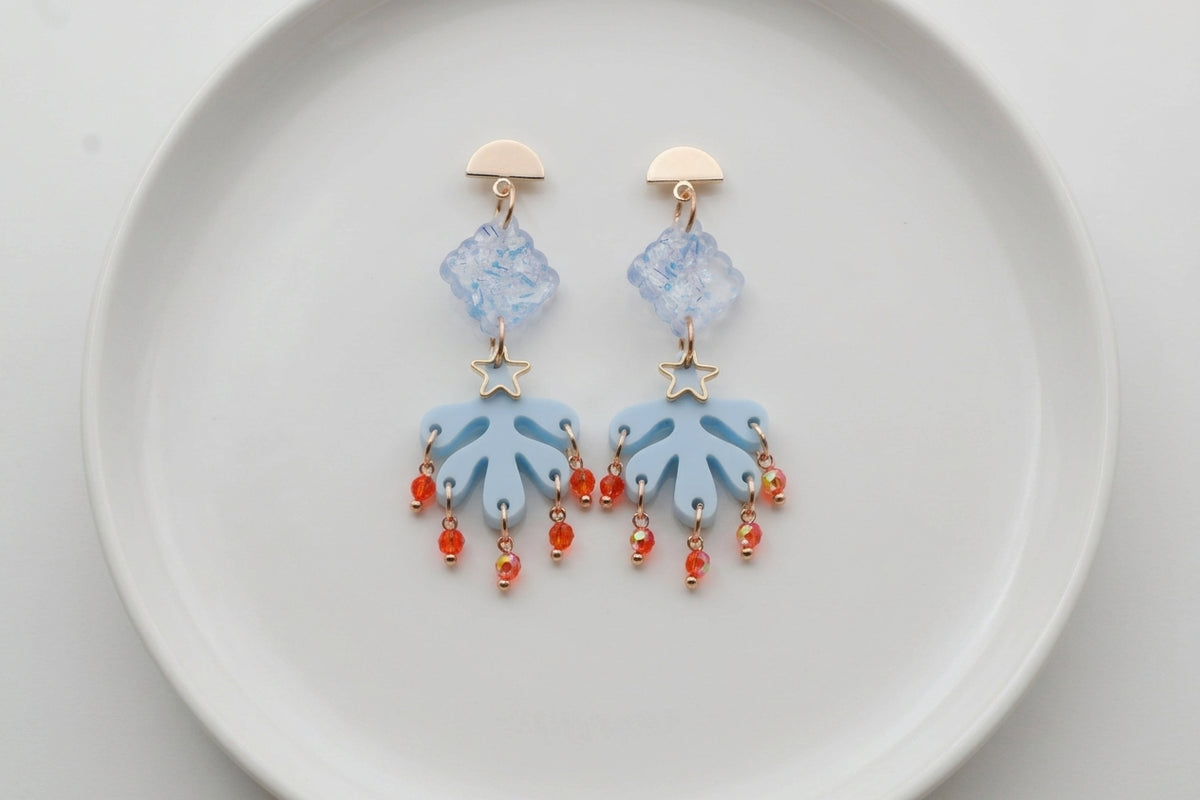 Blue Alba acrylic statement dangle earrings arranged on a white plate