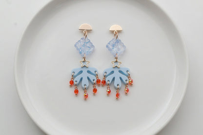Blue Alba acrylic statement dangle earrings arranged on a white plate