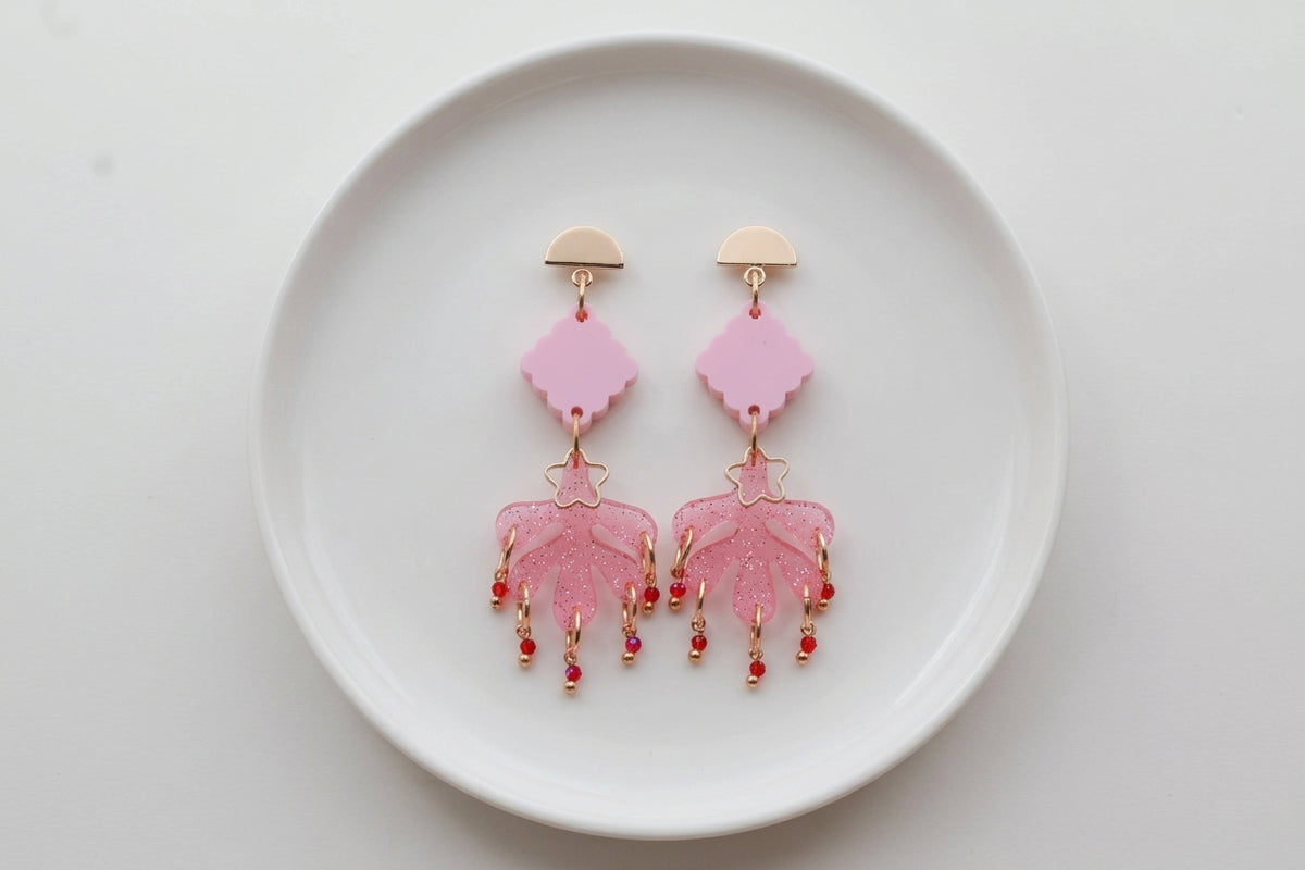 Pink Alba acrylic statement dangle earrings arranged on a white plate