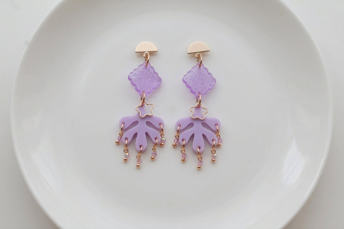 Purple Alba acrylic statement dangle earrings arranged on a white plate