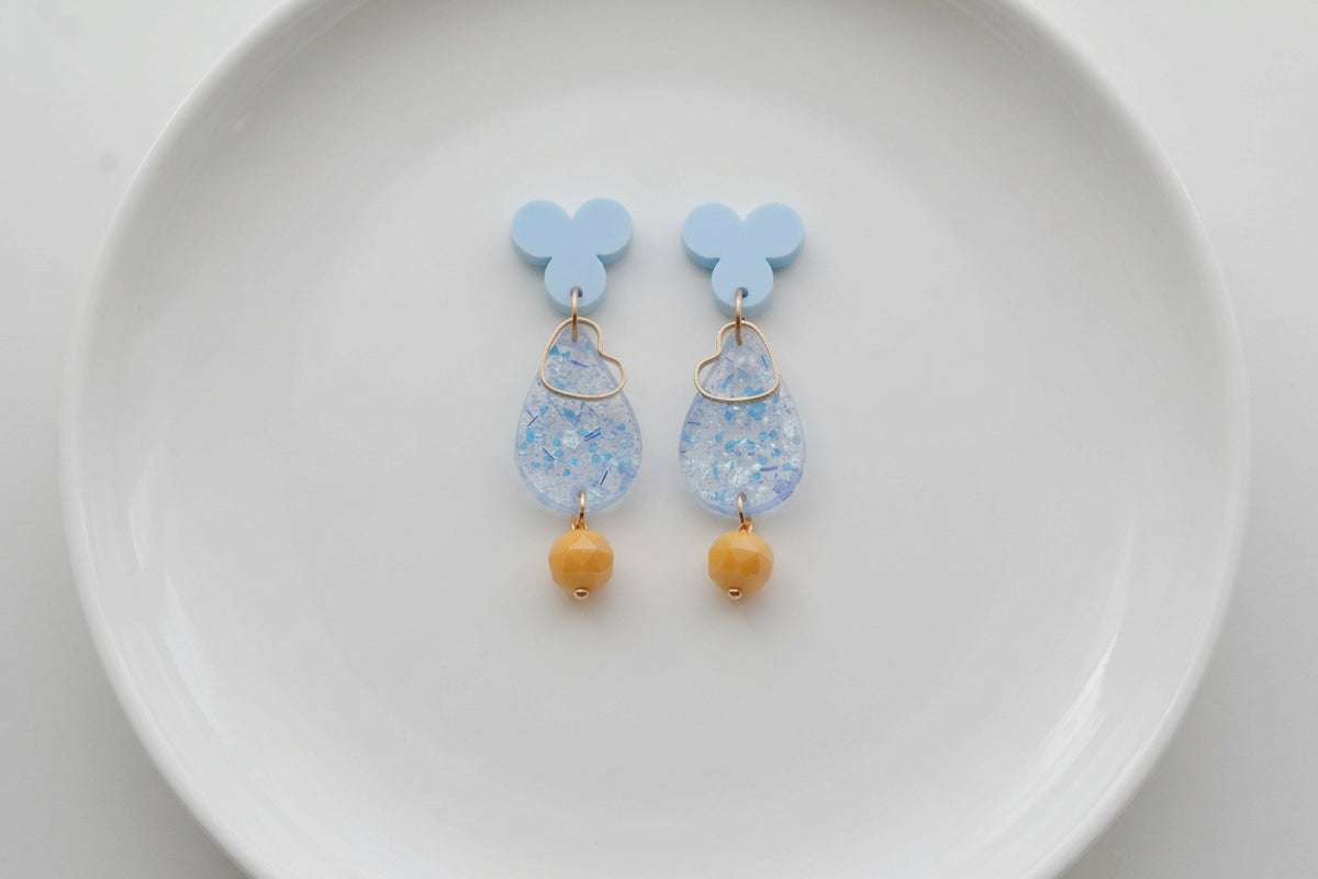 Blue Ana teardrop acrylic dangle earrings arranged on a white plate