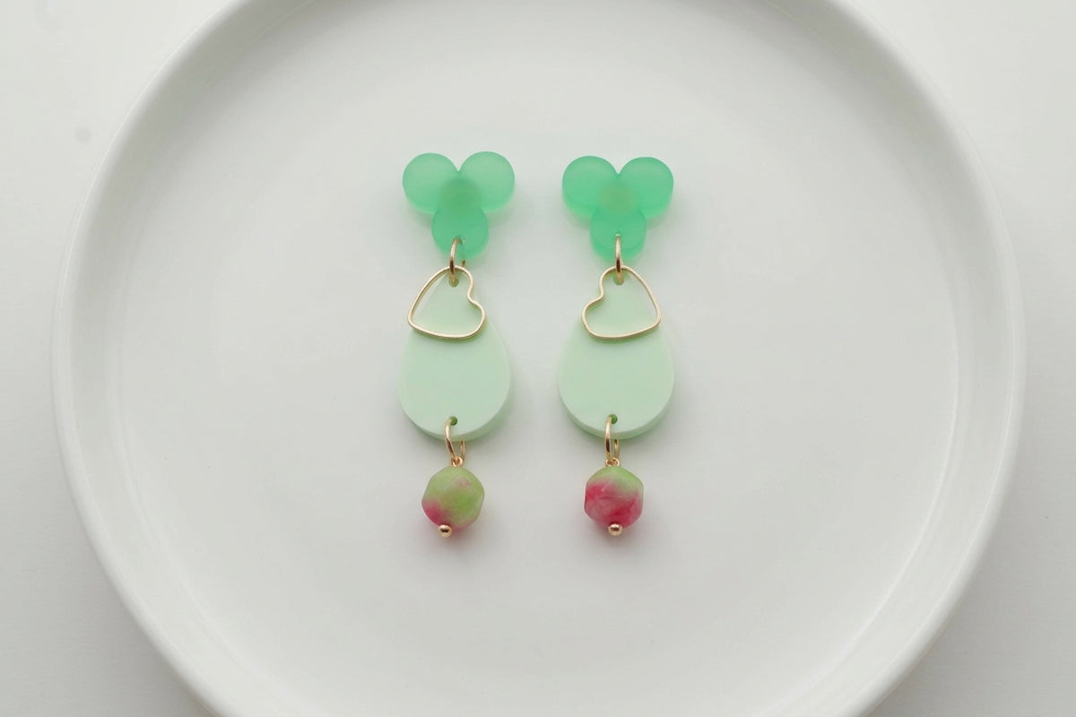 Green Ana teardrop acrylic dangle earrings arranged on a white plate