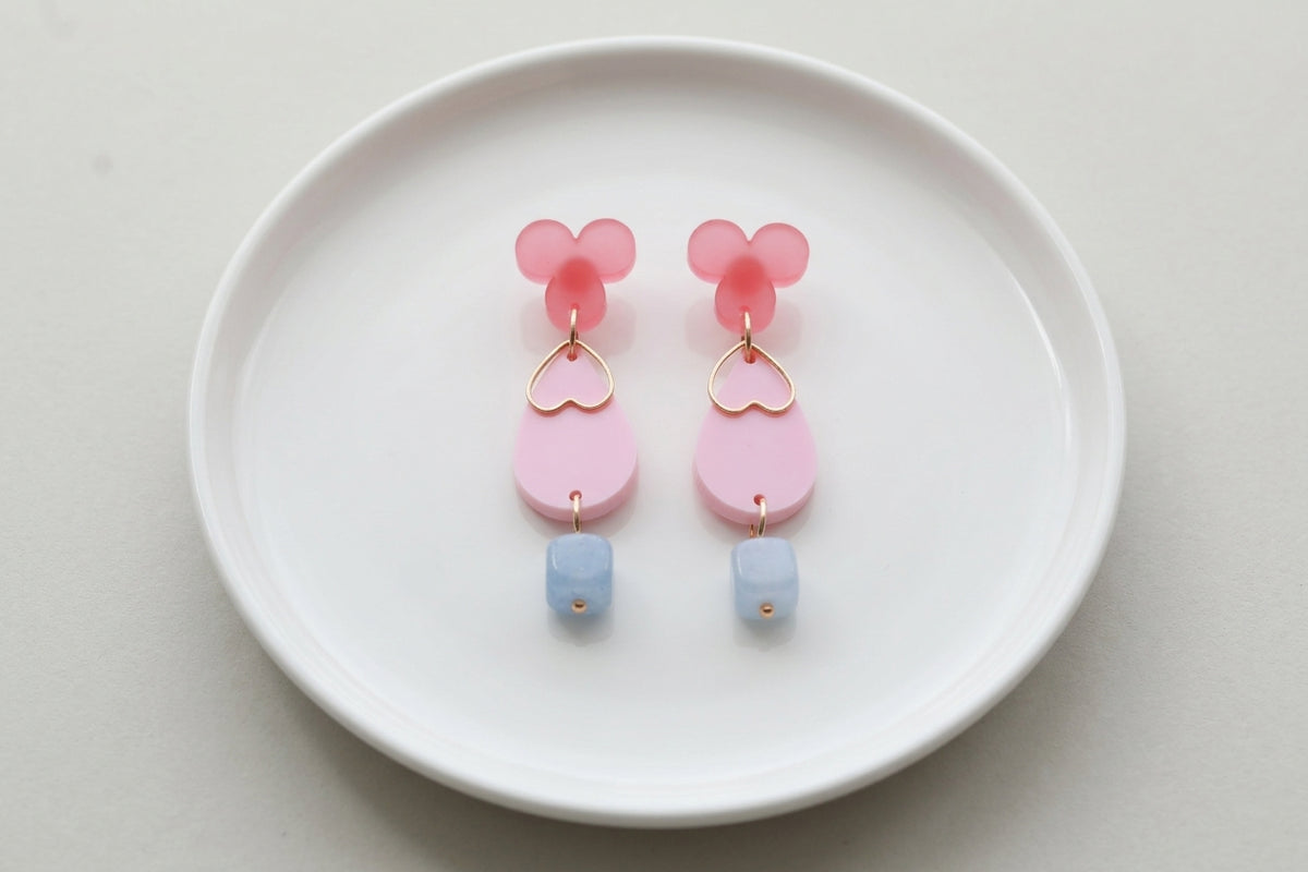 Pink Ana teardrop acrylic dangle earrings arranged on a white plate