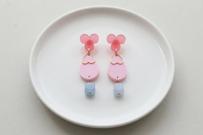Pink Ana teardrop acrylic dangle earrings arranged on a white plate