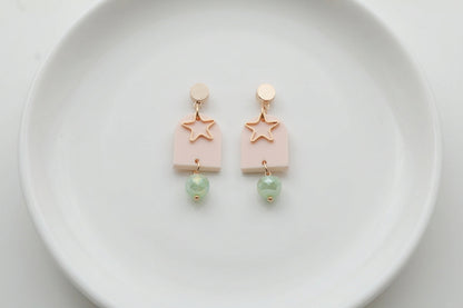 Beige Eira star acrylic drop earrings arranged on a white plate