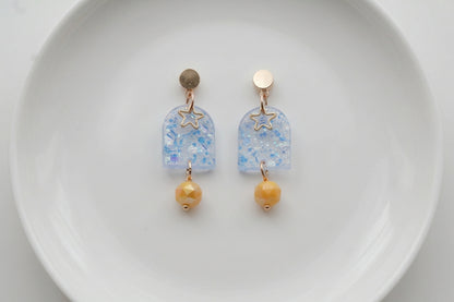 Blue Eira star acrylic drop earrings arranged on a white plate