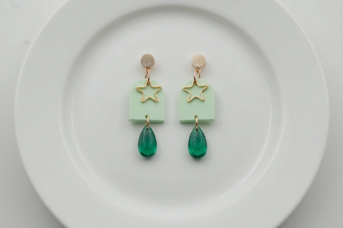 Green Eira star acrylic drop earrings arranged on a white plate