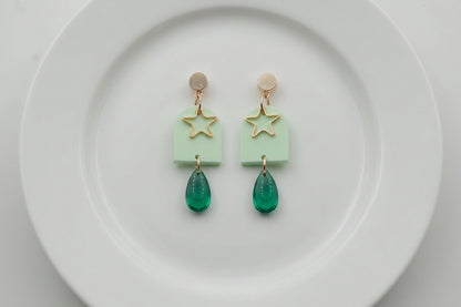 Green Eira star acrylic drop earrings arranged on a white plate