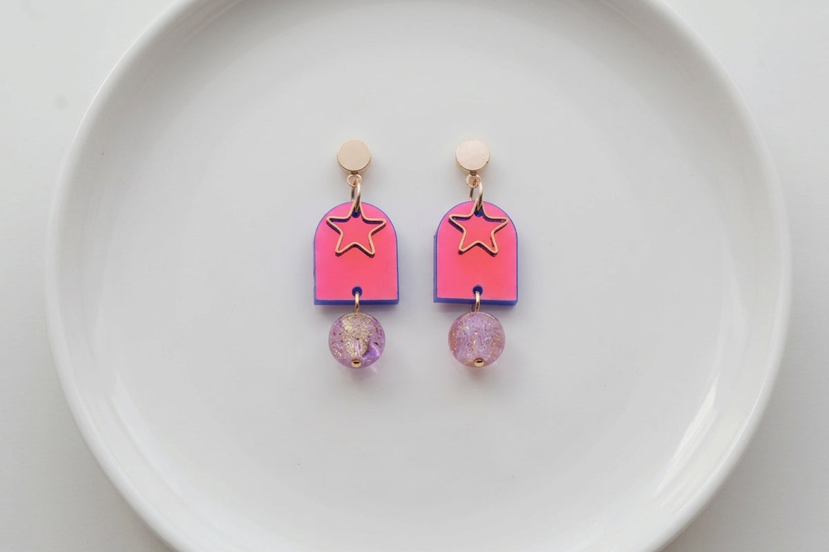 HB Eira star acrylic drop earrings arranged on a white plate