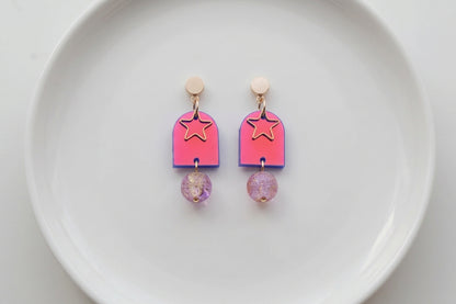 HB Eira star acrylic drop earrings arranged on a white plate