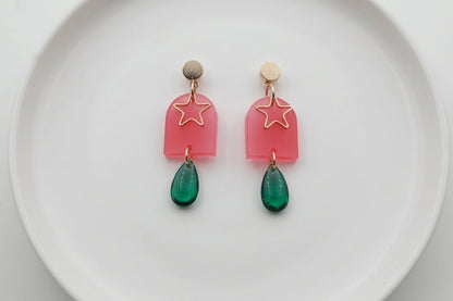 Pink Eira star acrylic drop earrings arranged on a white plate