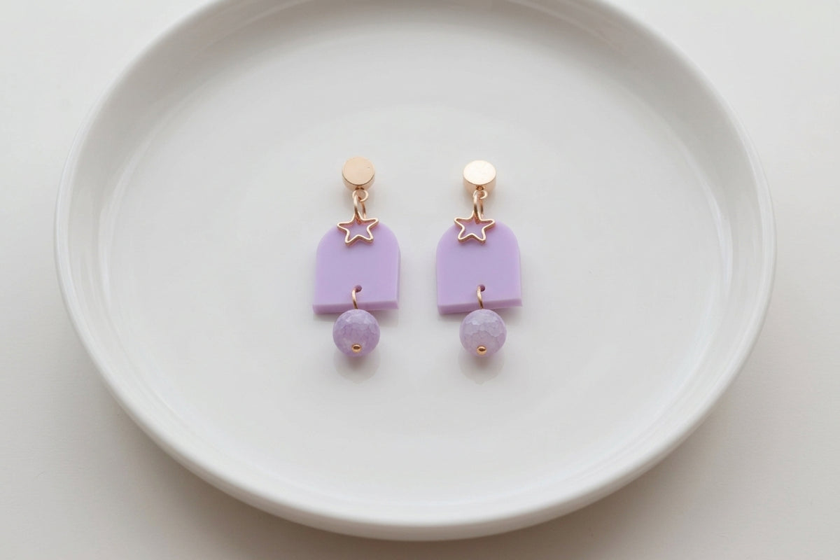 Purple Eira star acrylic drop earrings arranged on a white plate