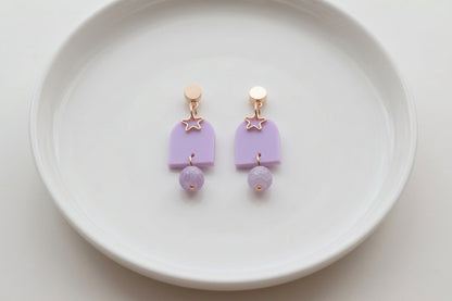 Purple Eira star acrylic drop earrings arranged on a white plate