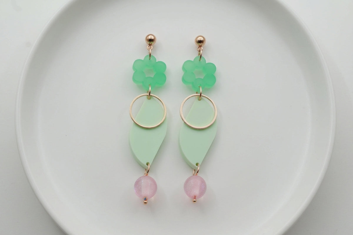 Green Elsa floral long dangle earrings arranged on a white plate