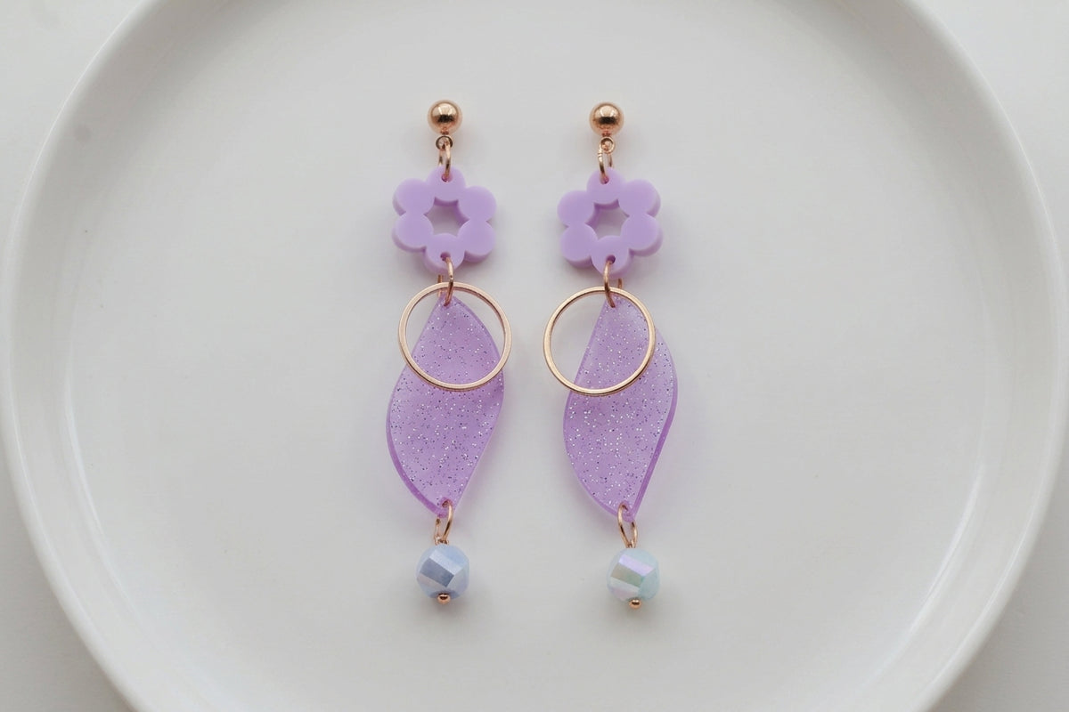 Purple Elsa floral long dangle earrings arranged on a white plate