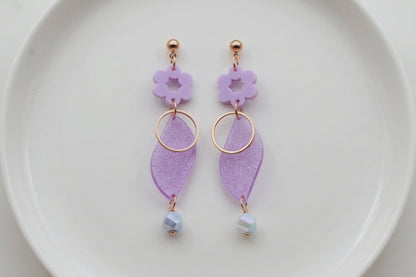 Purple Elsa floral long dangle earrings arranged on a white plate