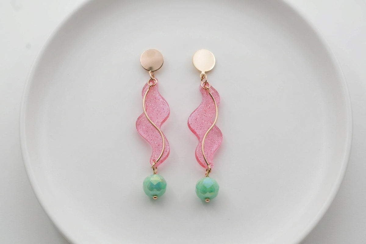 Pink Esme long acrylic statement earrings arranged on a white plate