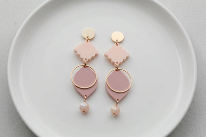 Beige Fien long geometric drop earrings arranged on a white plate
