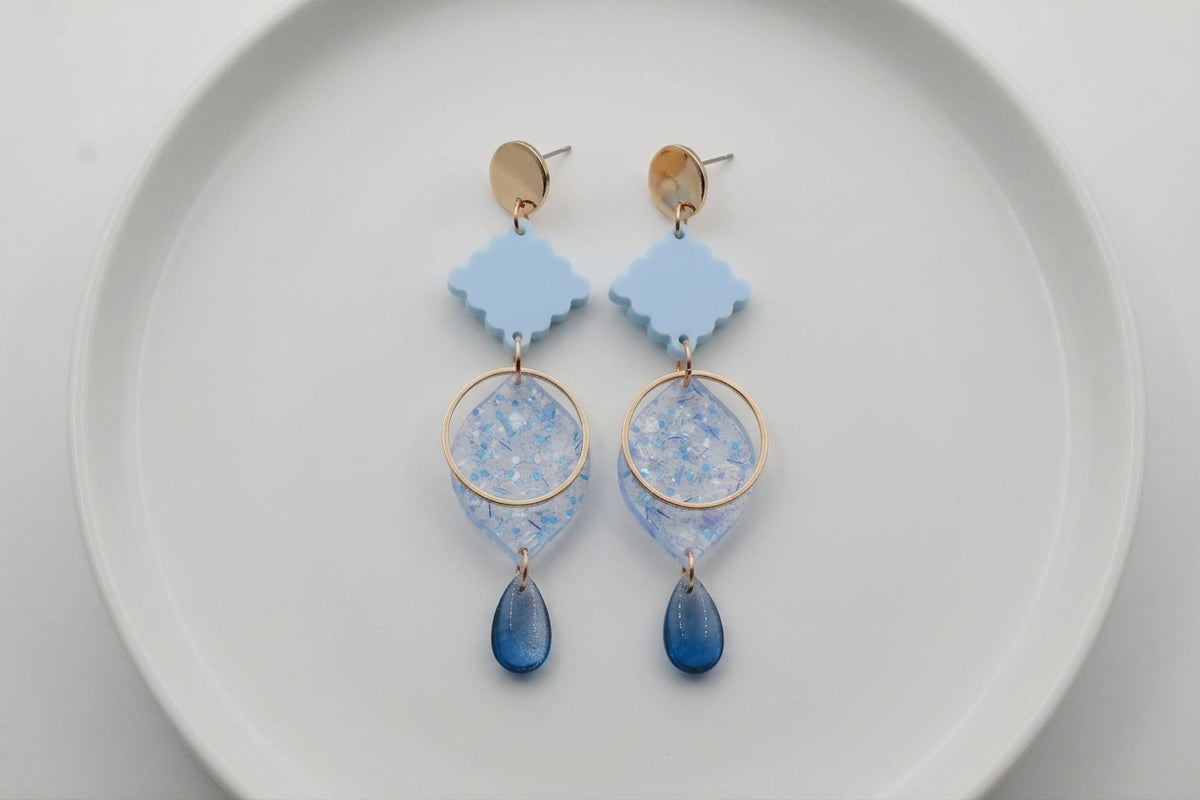 Blue Fien long geometric drop earrings arranged on a white plate