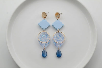 Blue Fien long geometric drop earrings arranged on a white plate