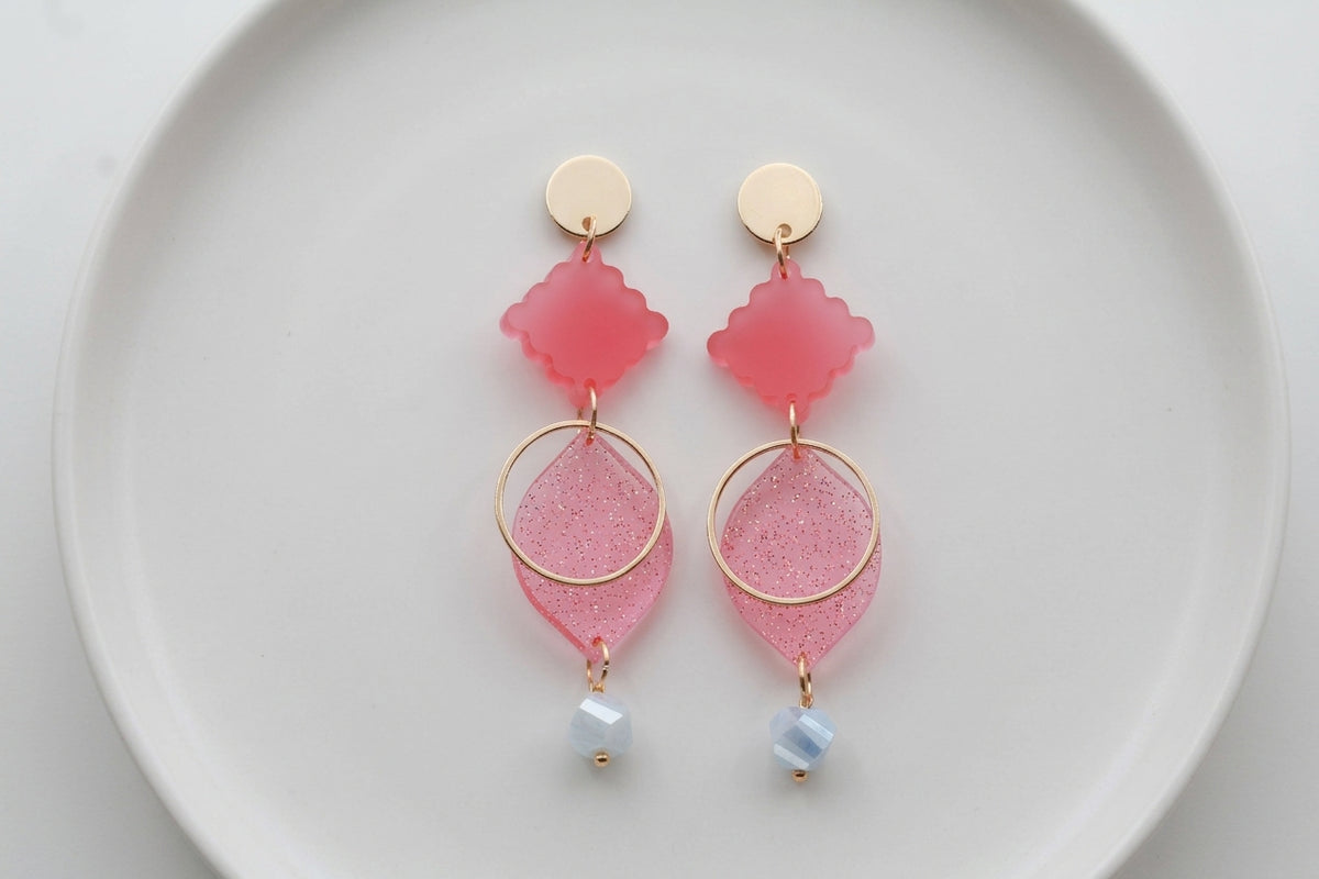 Pink Fien long geometric drop earrings arranged on a white plate