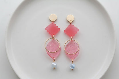 Pink Fien long geometric drop earrings arranged on a white plate