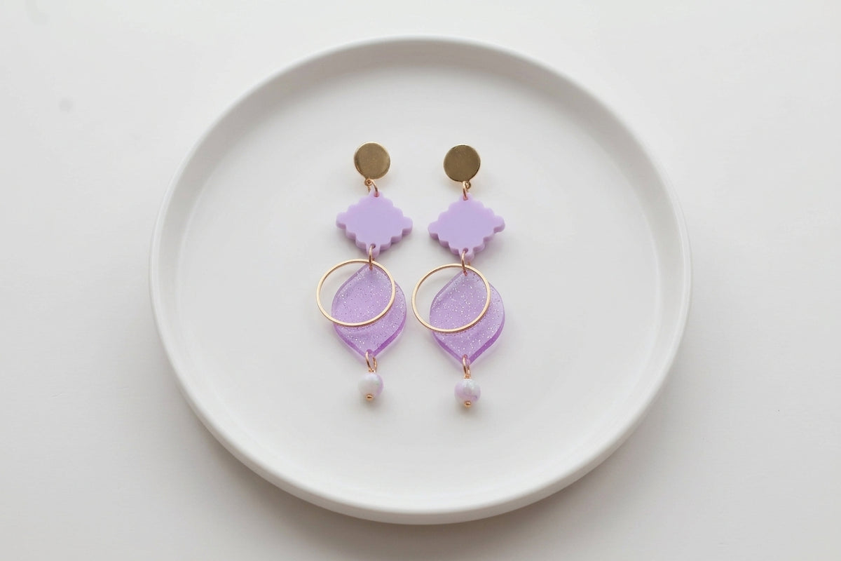 Purple Fien long geometric drop earrings arranged on a white plate