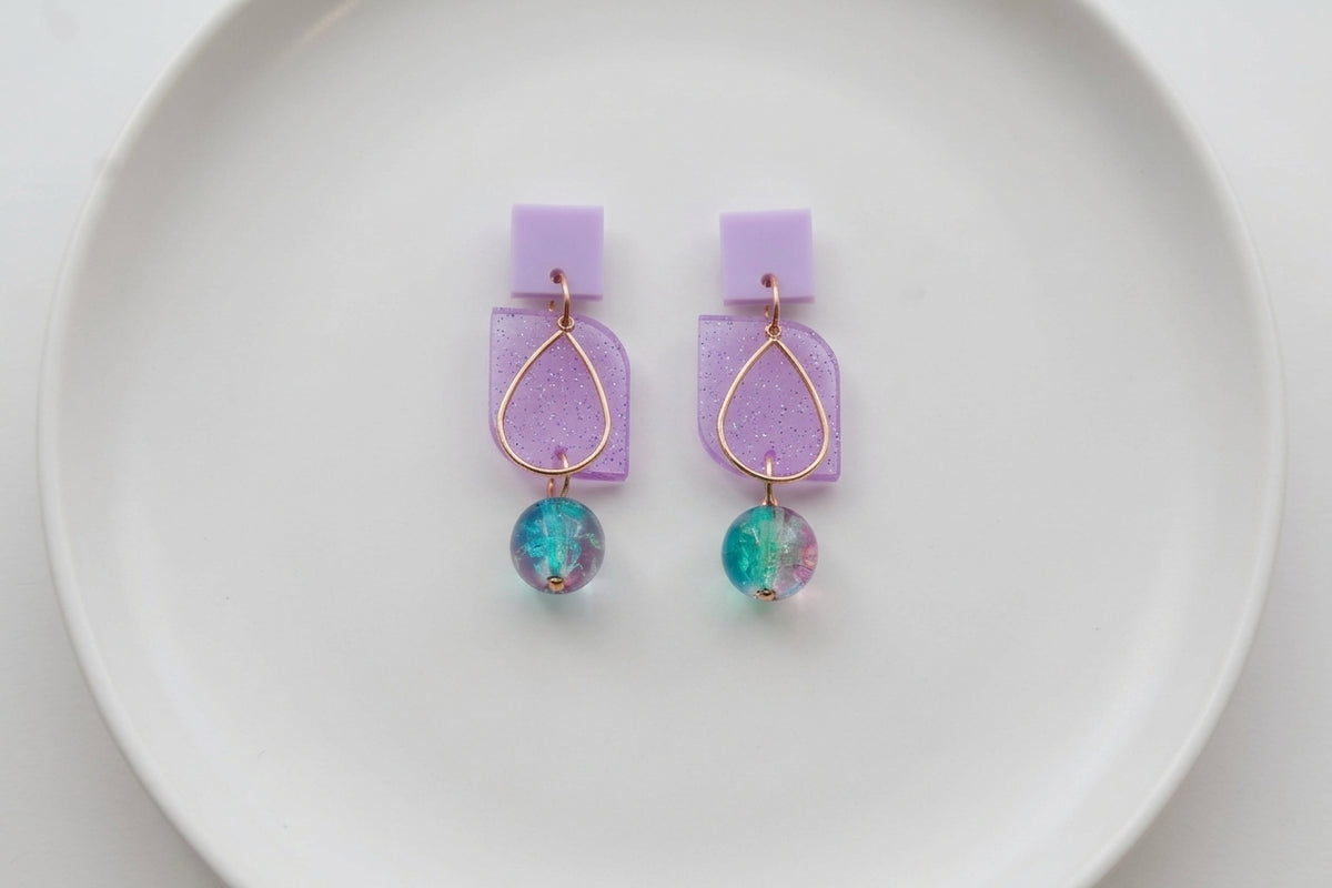 Purple Freya small geometric dangle earrings arranged on a white plate