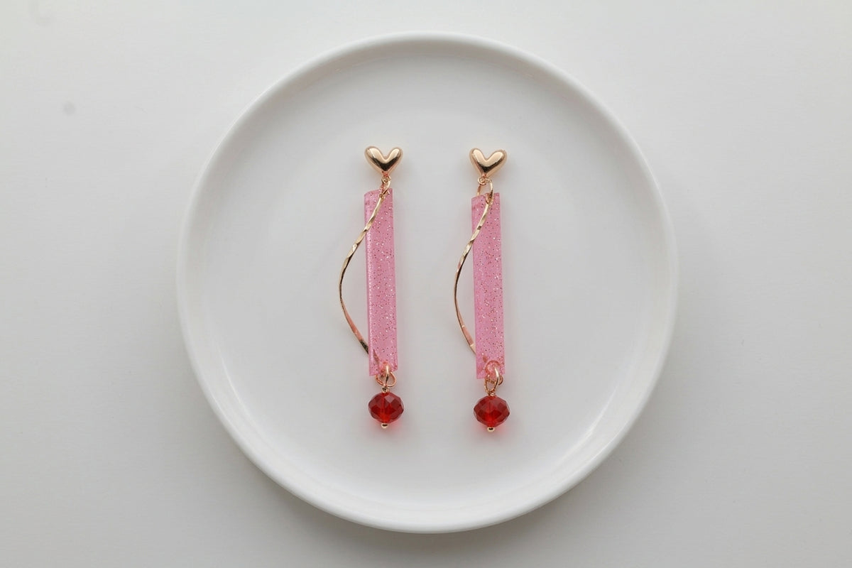 Pink Ina long rectangle acrylic earrings arranged on a white plate