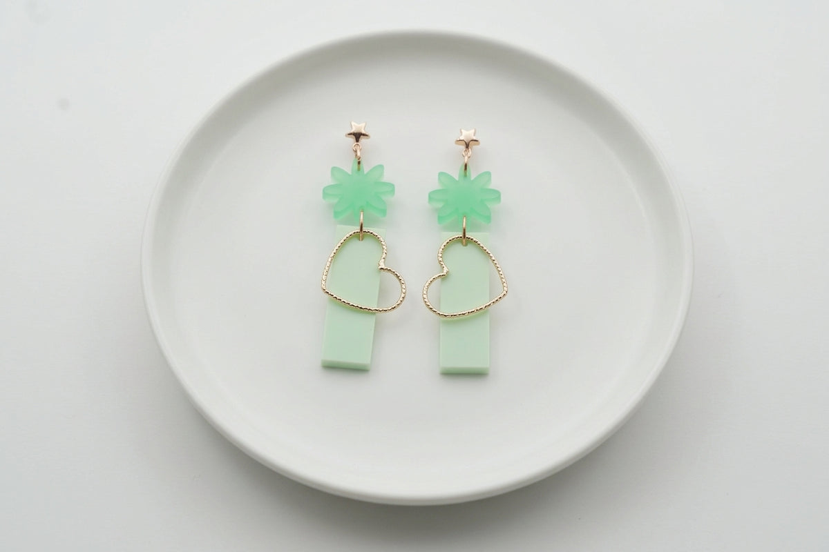 Green Ines floral heart dangle earrings arranged on a white plate