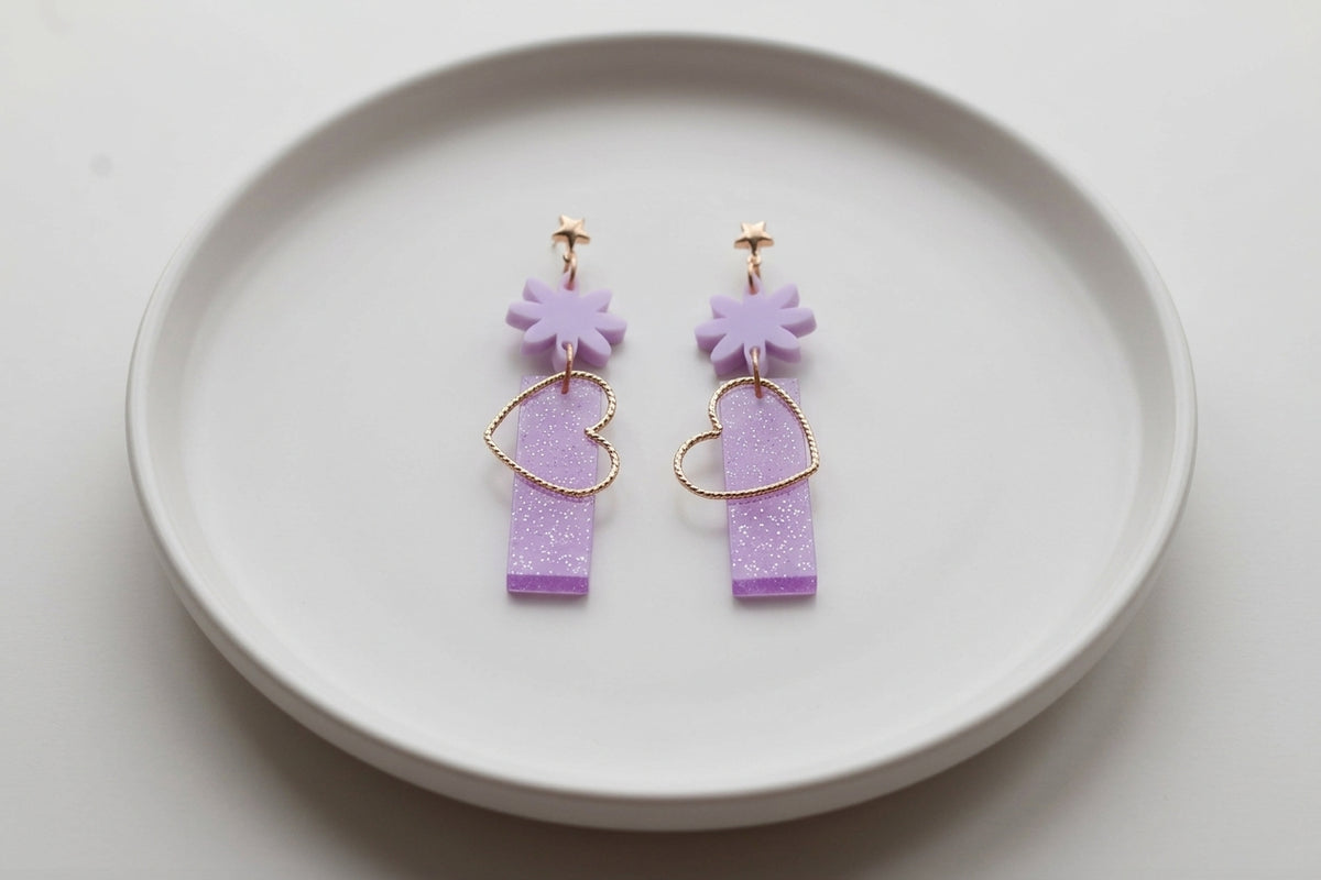 Purple Ines floral heart dangle earrings arranged on a white plate