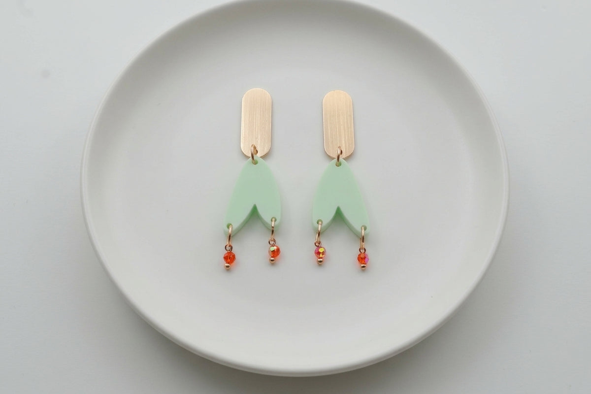 Green Iris geometric long drop earrings arranged on a white plate