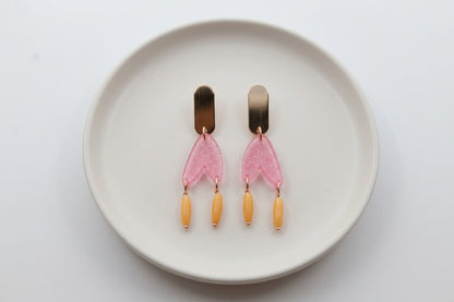 Pink Iris geometric long drop earrings arranged on a white plate