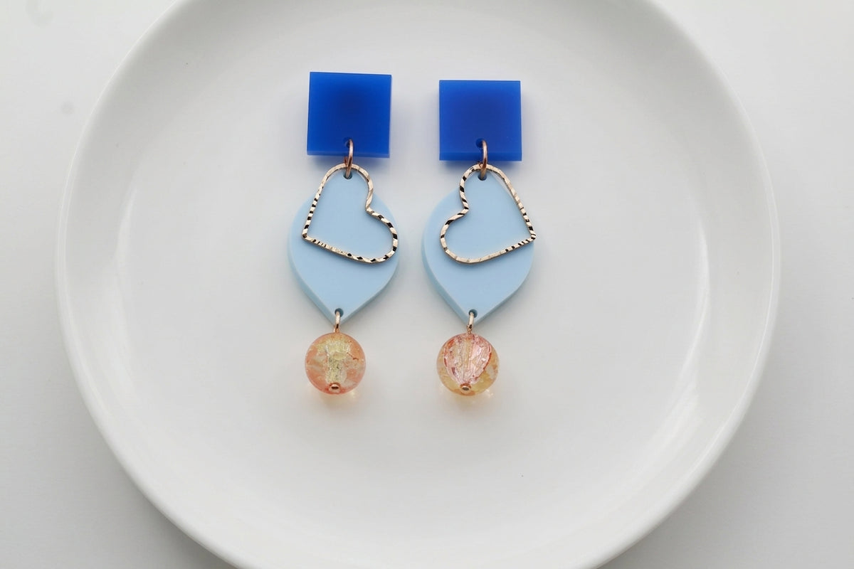 Blue Lara heart acrylic dangle earrings arranged on a white plate