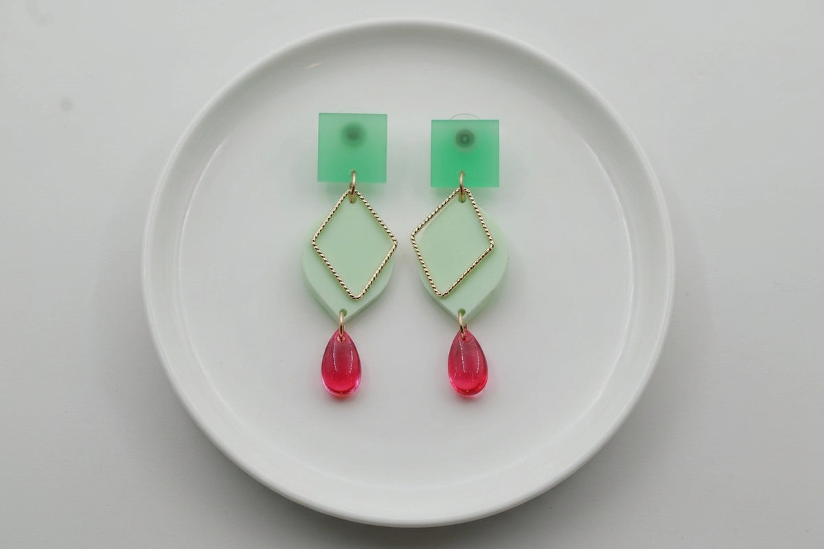 Green Lara heart acrylic dangle earrings arranged on a white plate
