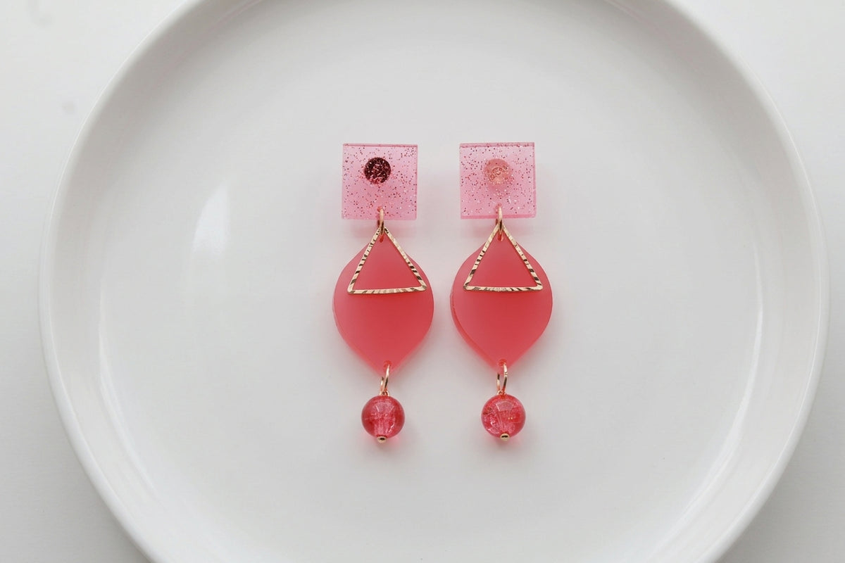 Pink Lara heart acrylic dangle earrings arranged on a white plate
