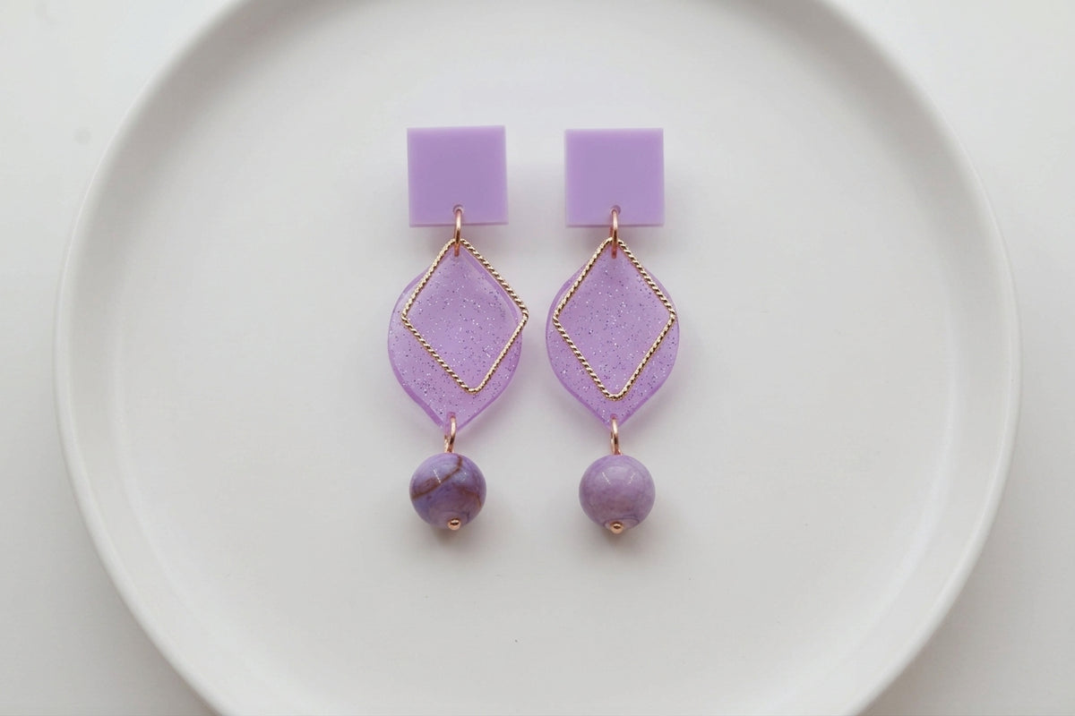 Purple Lara heart acrylic dangle earrings arranged on a white plate