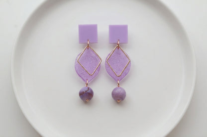 Purple Lara heart acrylic dangle earrings arranged on a white plate