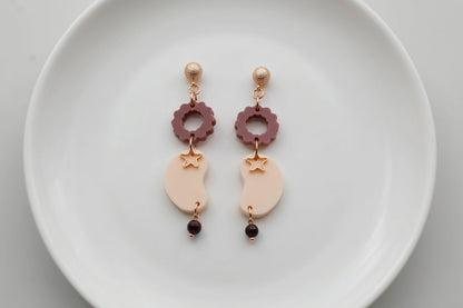 Beige Lucia floral star dangle earrings arranged on a white plate