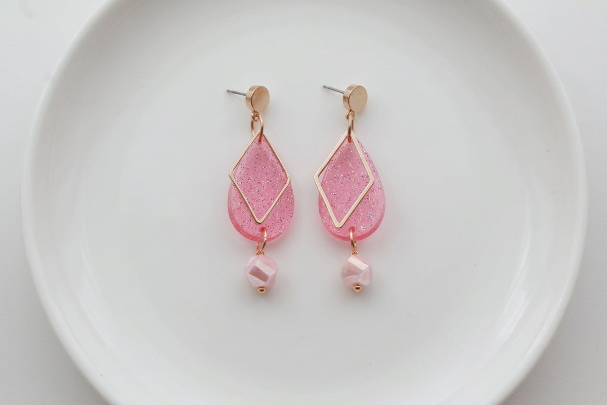 Pink Mia geometric teardrop earrings arranged on a white plate