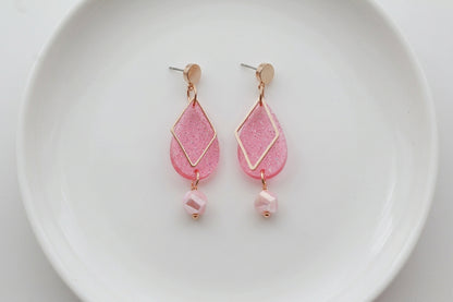 Pink Mia geometric teardrop earrings arranged on a white plate