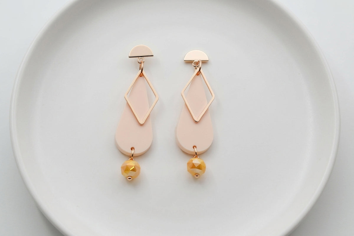 Beige Mila teardrop statement earrings arranged on a white plate