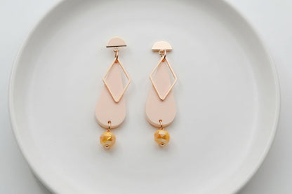 Beige Mila teardrop statement earrings arranged on a white plate