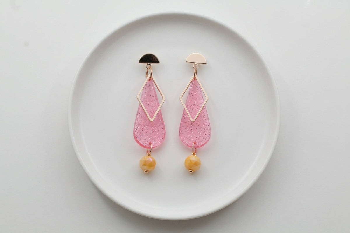 Pink Mila teardrop statement earrings arranged on a white plate