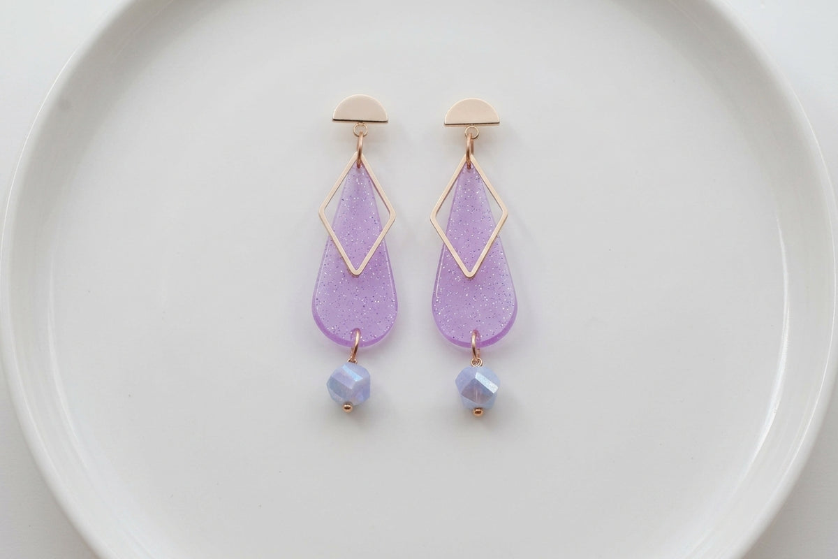 Purple Mila teardrop statement earrings arranged on a white plate