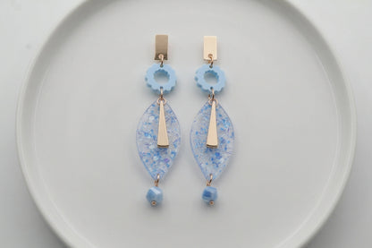 Blue Nia long geometric statement earrings arranged on a white plate